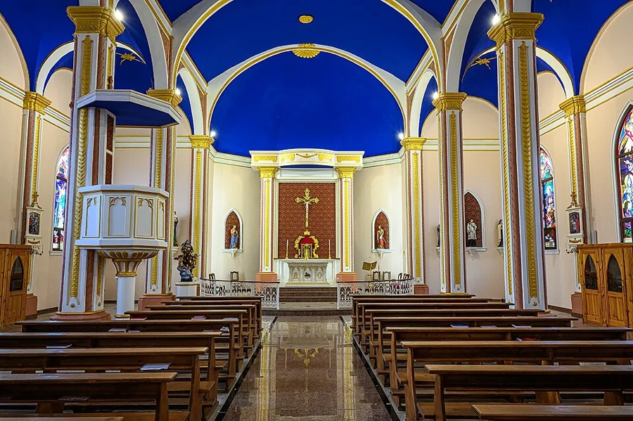 Interior de uma igreja católica com teto azul e nave central