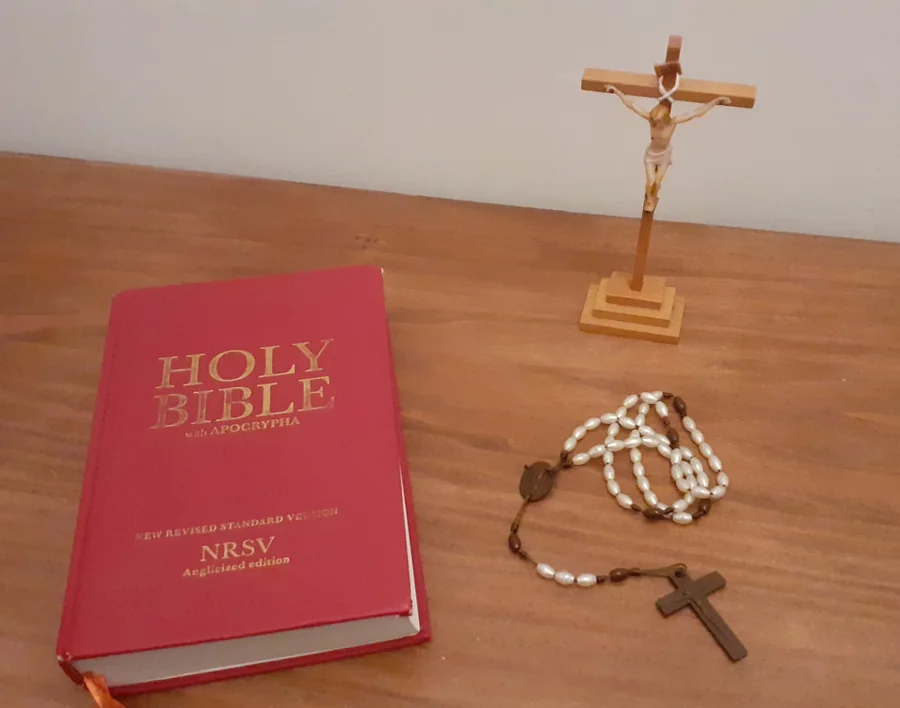 Crucifixo, terço e Bíblia sobre uma mesa de madeira